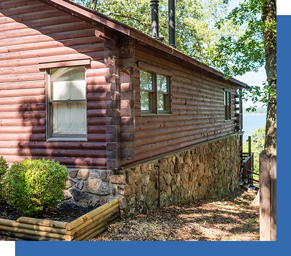 A log cabin with a stone wall and trees.